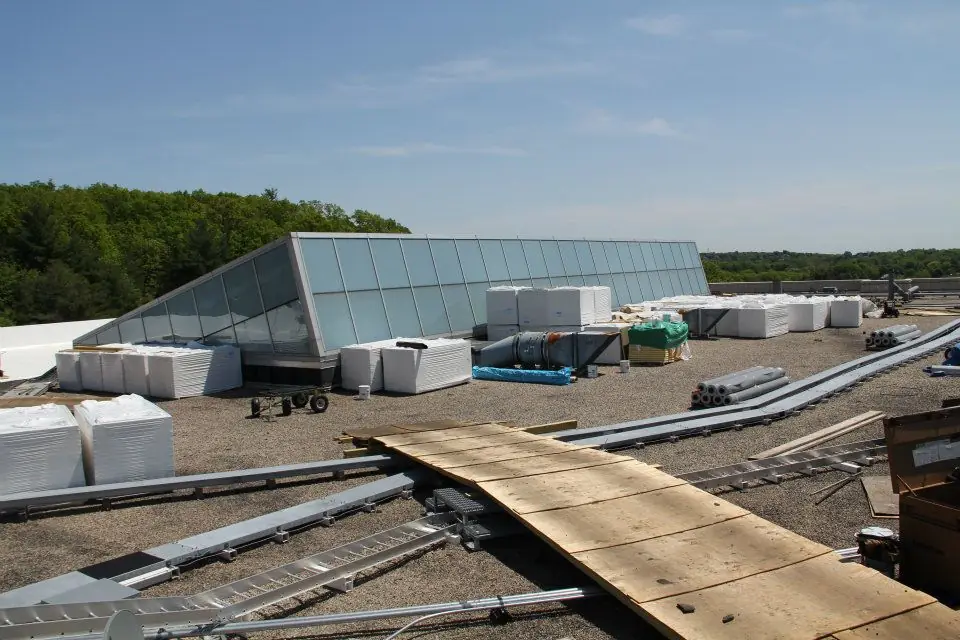 Rooftop skylight structure with a plank ramp and stacked materials on a ballast roof