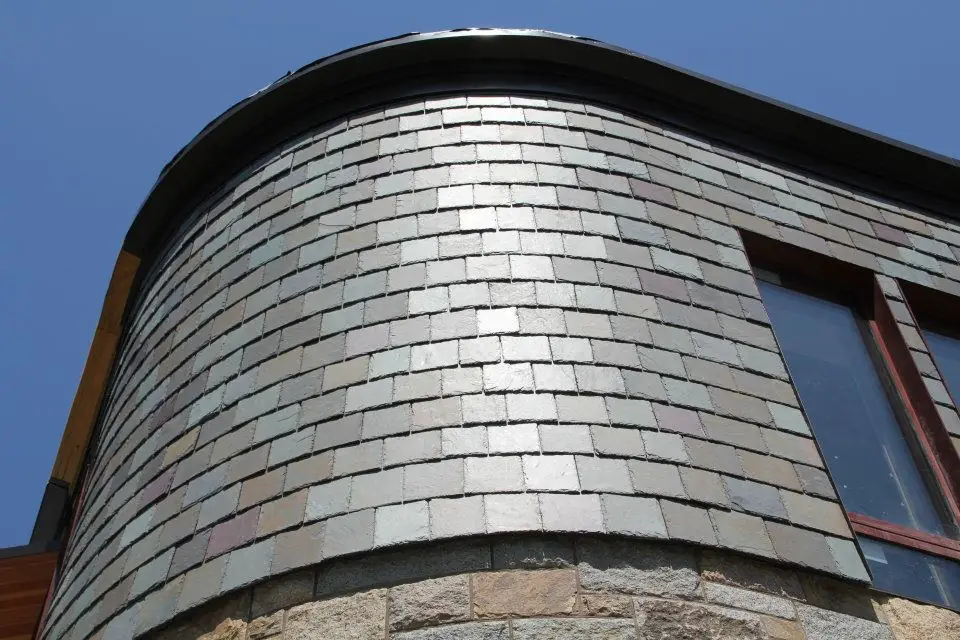 Curved turret wall clad in grey slate under a clear blue sky