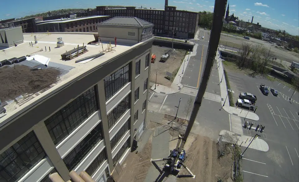 Crane boom lifting roofing material onto the flat roof of a brick mill building