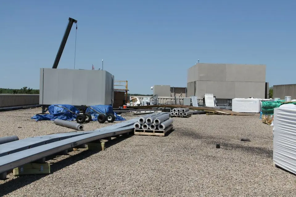 Ballasted commercial roof with a rooftop unit, pipe stacks and a crane on the skyline