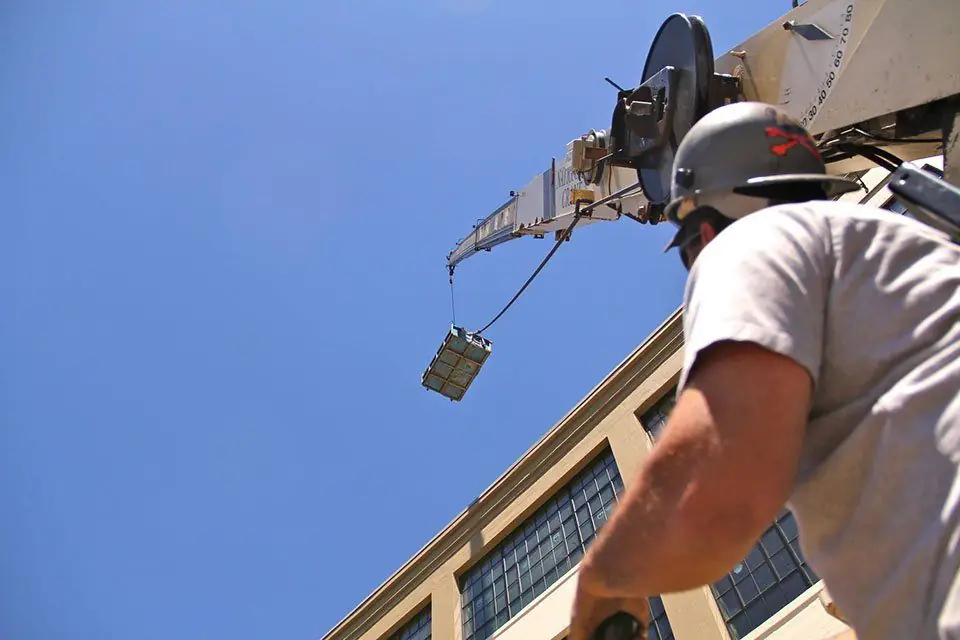 Roofer in a hard hat guiding a crane load onto a building roof