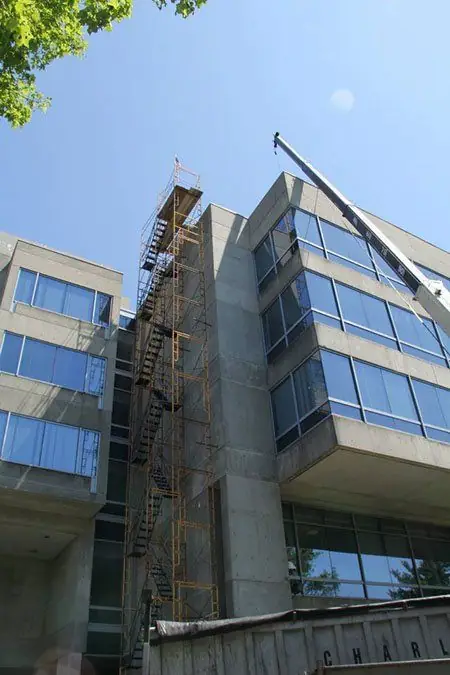 Scaffolding against a glass and brick building with a crane arm overhead