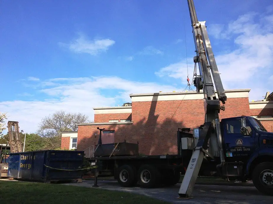 A&M boom crane truck loading roofing material beside a brick school building